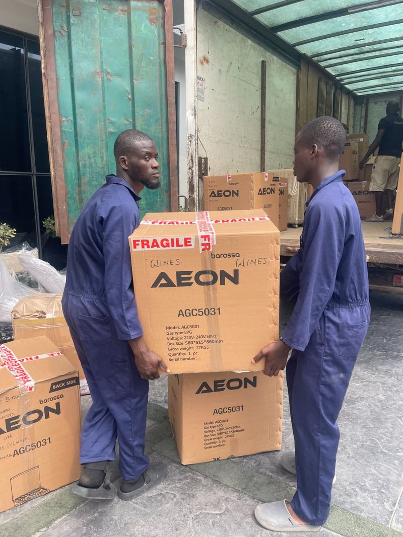 Two movers carrying a carton sealed with fragile tape and hand-labelled wines, showing how Pack n Moove labels boxes room by room