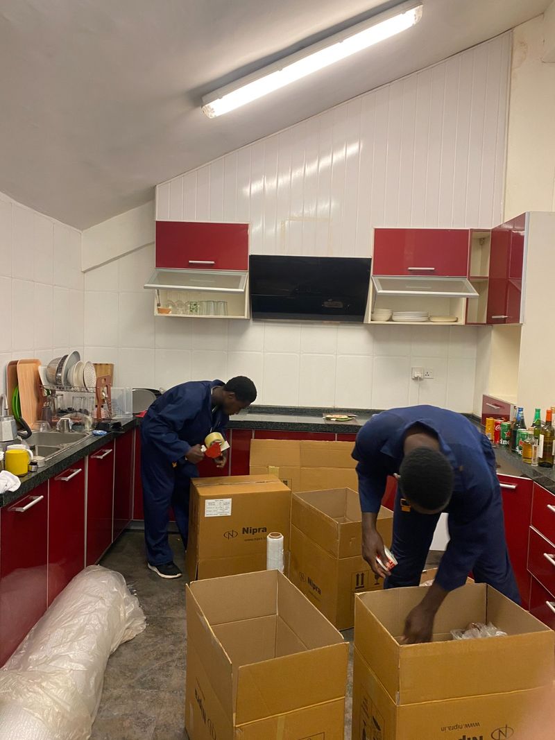 Two Pack n Moove movers packing kitchen plates and glassware into cartons before a house move