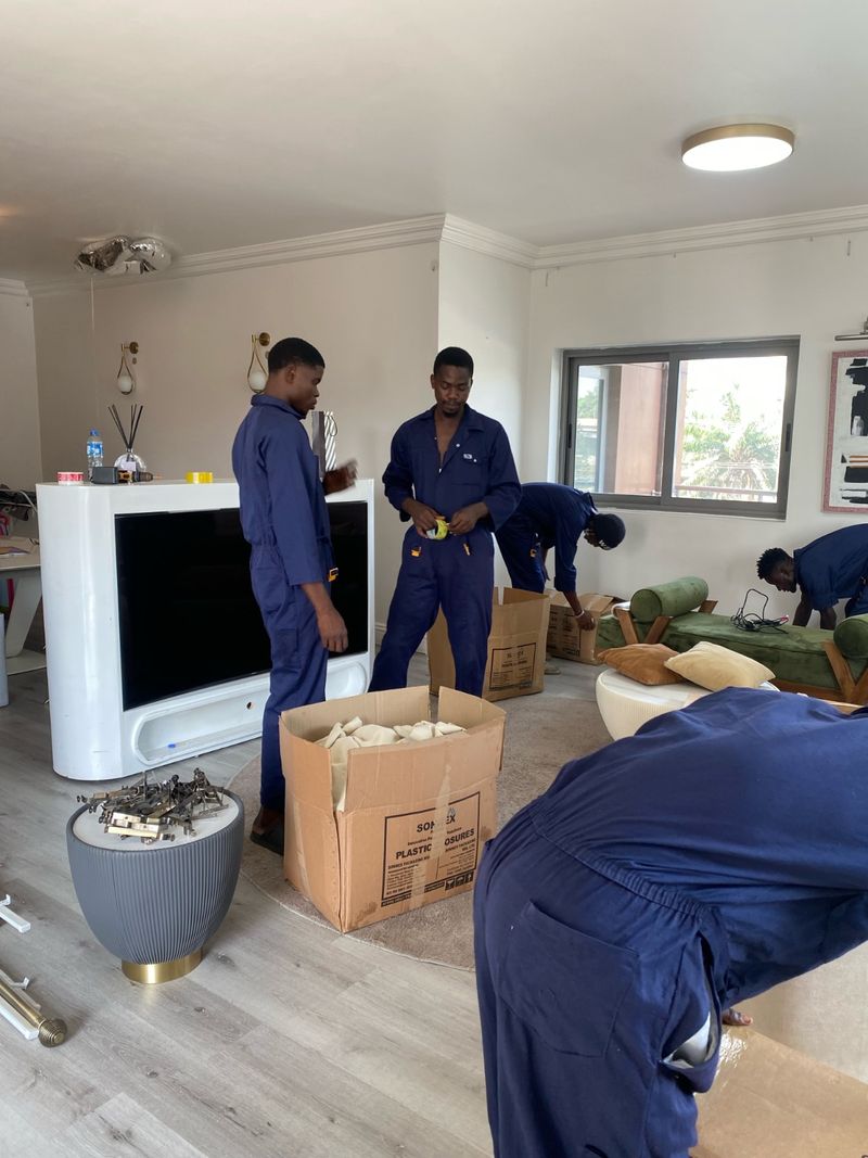 Moving crew disassembling a TV console and packing office furniture during a commercial relocation in Lagos