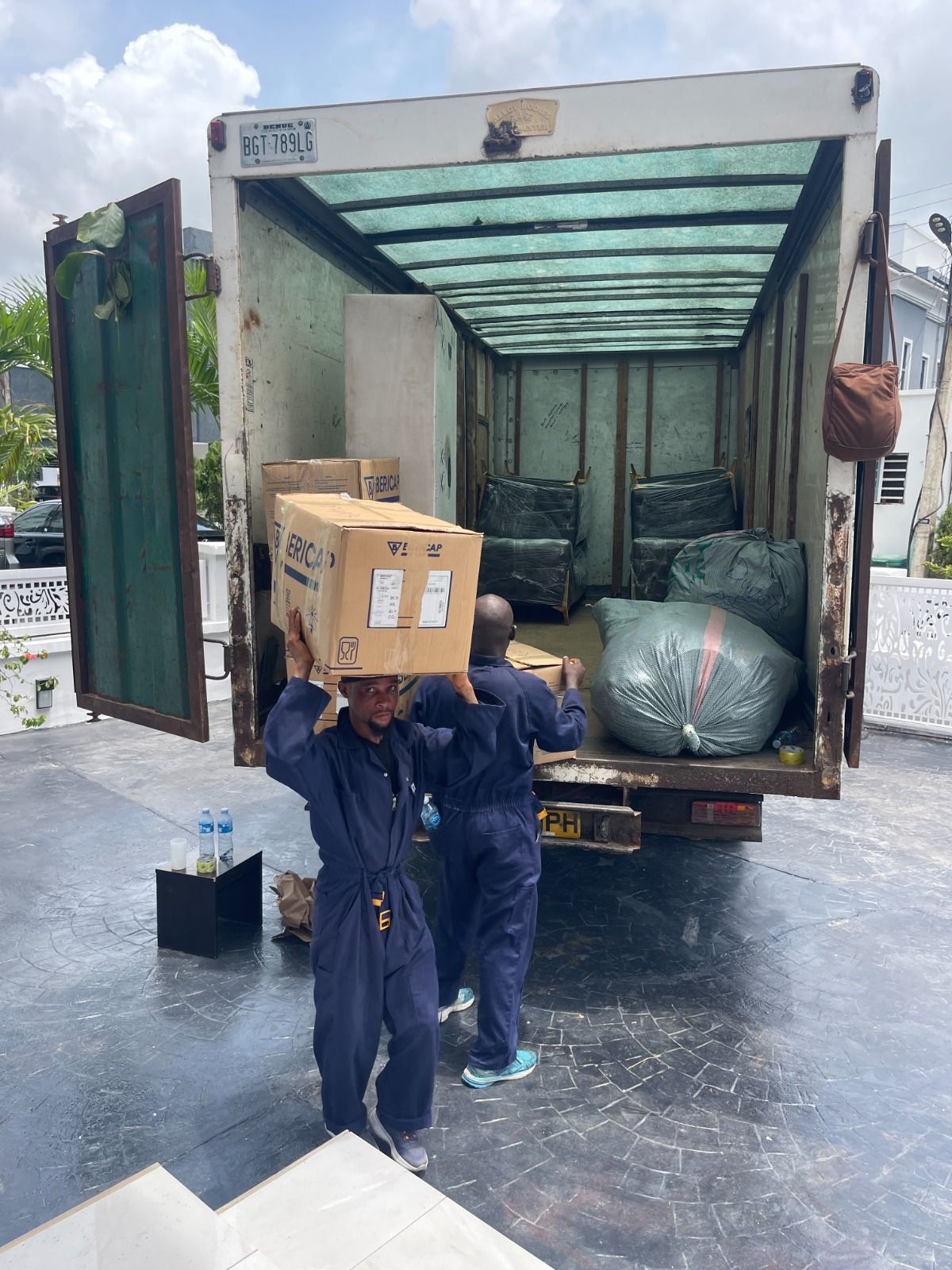Pack n Moove mover carrying a carton on his shoulder while unloading a fully packed moving truck at a Lagos residence
